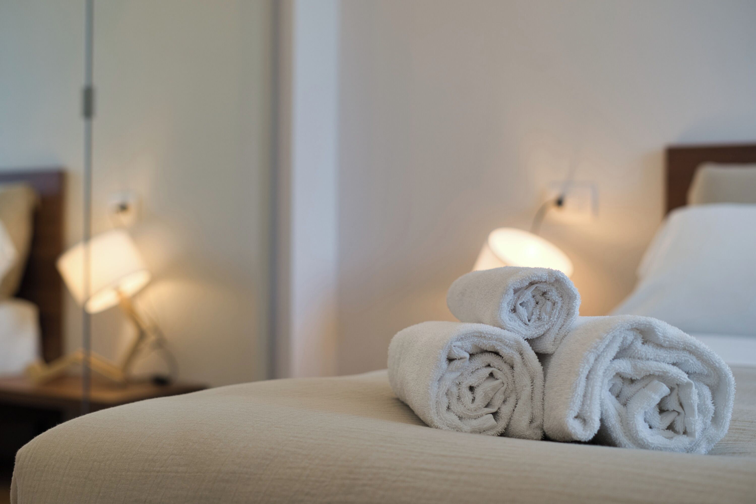 Un lit bien fait, avec des serviettes blanches pliées en rouleaux et une lampe de chevet.