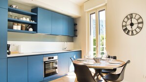 A modern kitchen with blue cabinets, a wooden dining table, and a black clock on the wall.