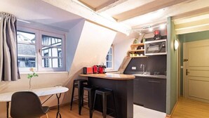 Una cocina compacta con barra, una mesa de comedor con dos sillas y un ventanal con cortinas.