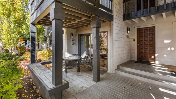 A covered porch with a table and chairs, a wooden deck, and a door with a number.