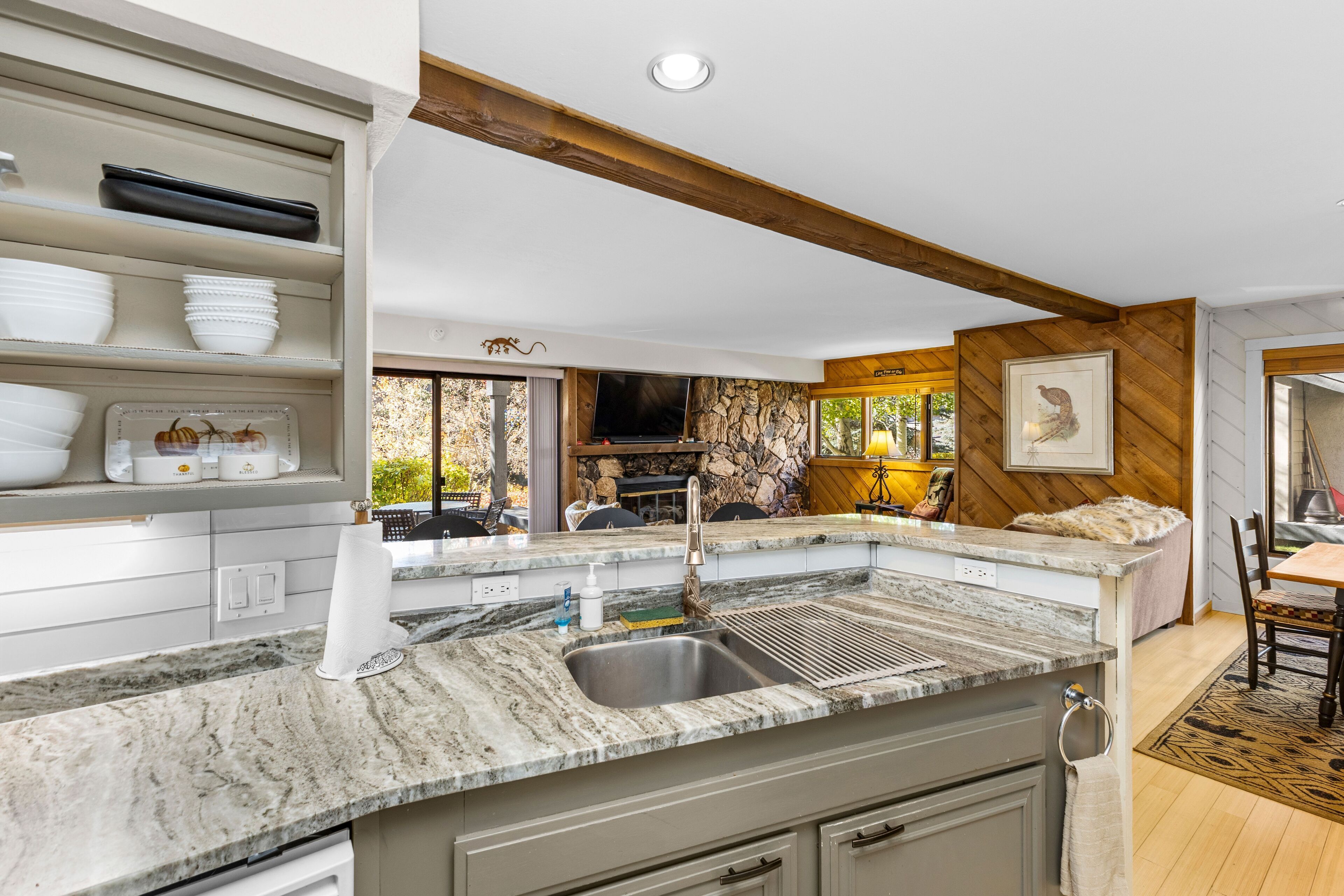 A kitchen with a granite countertop, a sink, and a stone backsplash. There is a dining area with a table and chairs.