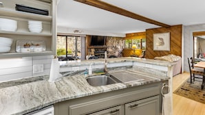 A kitchen with a granite countertop, a sink, and a stone backsplash. There is a dining area with a table and chairs.