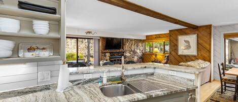 A kitchen with a granite countertop, a sink, and a stone backsplash. There is a dining area with a table and chairs.