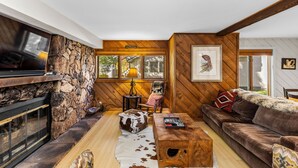 A cozy living room with a stone fireplace, a wooden ceiling, and a large window.