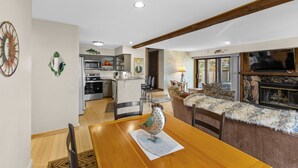 A spacious living area with a wooden dining table, a decorative bird sculpture, and a stone fireplace.
