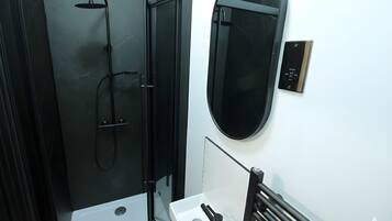 A modern bathroom with a glass-enclosed shower, a white sink, and a black towel rack.