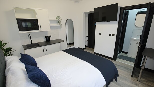 A modern hotel room with a bed, a kitchenette, a bathroom, and a TV.
