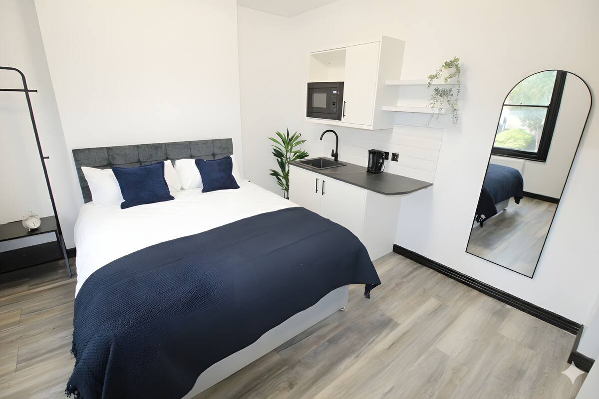 A modern bedroom with a bed, a small kitchenette, and a large mirror.