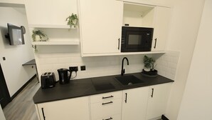 A modern kitchen with white cabinets, a black countertop, a microwave, a sink, and a toaster.