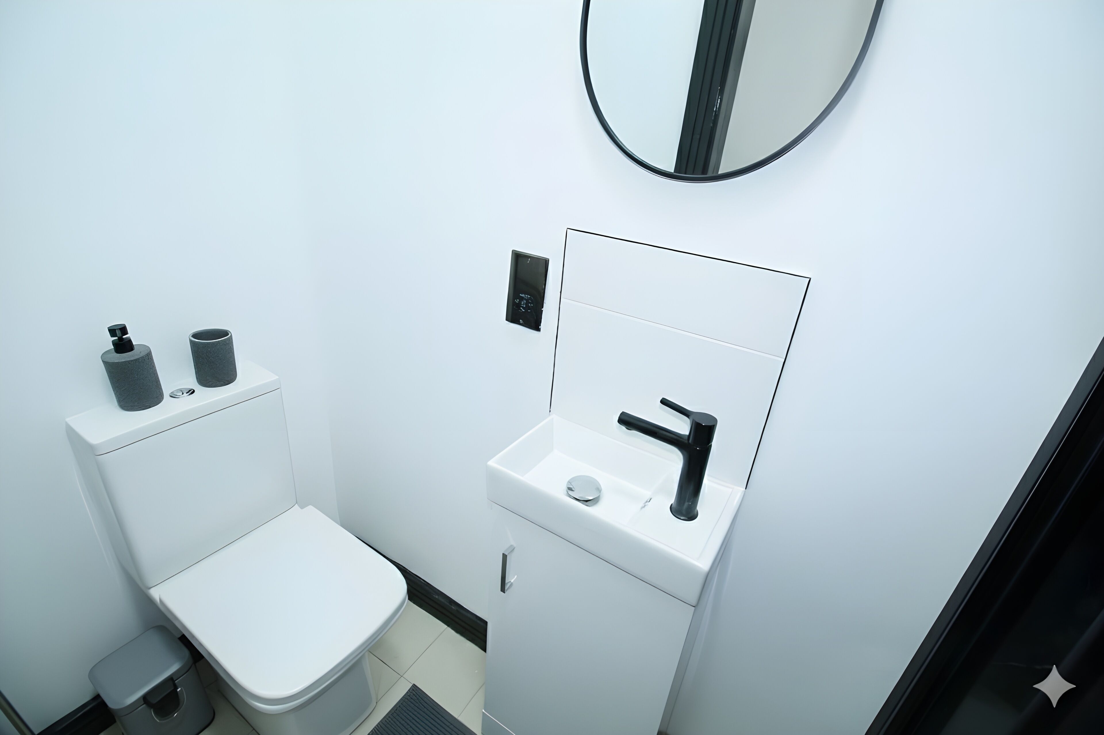 A compact bathroom with a white toilet, a sink with a mirror, and a small trash bin.