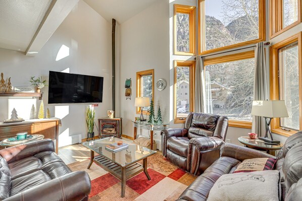 A spacious living room with leather sofas, a glass coffee table, a fireplace, and large windows offering a view of a snowy landscape. - Ouray Getaway: Walk to Hot Springs, Trails & Shops (Ouray)