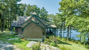 A cabin with a stone chimney, a porch, and a view of a lake surrounded by trees. - Windward Lodge- stunning, dog-friendly private waterfront retreat. Seasonal dock (Woolwich)