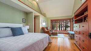 A bedroom with a large bed, a wooden dresser, and a seating area with a chair and ottoman. - Windward Lodge- stunning, dog-friendly private waterfront retreat. Seasonal dock (Woolwich)