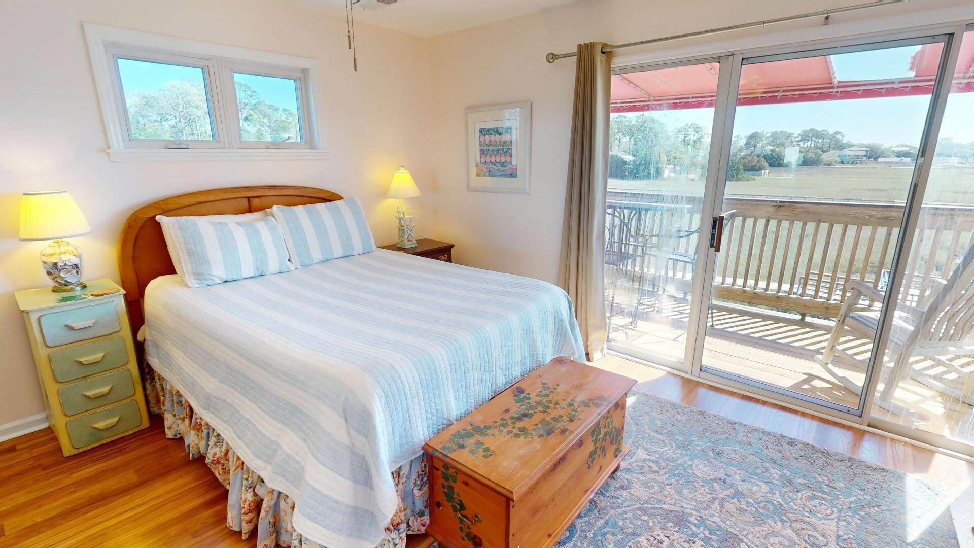A bedroom with a bed, bedside lamps, a wooden chest, and a view of an outdoor deck.