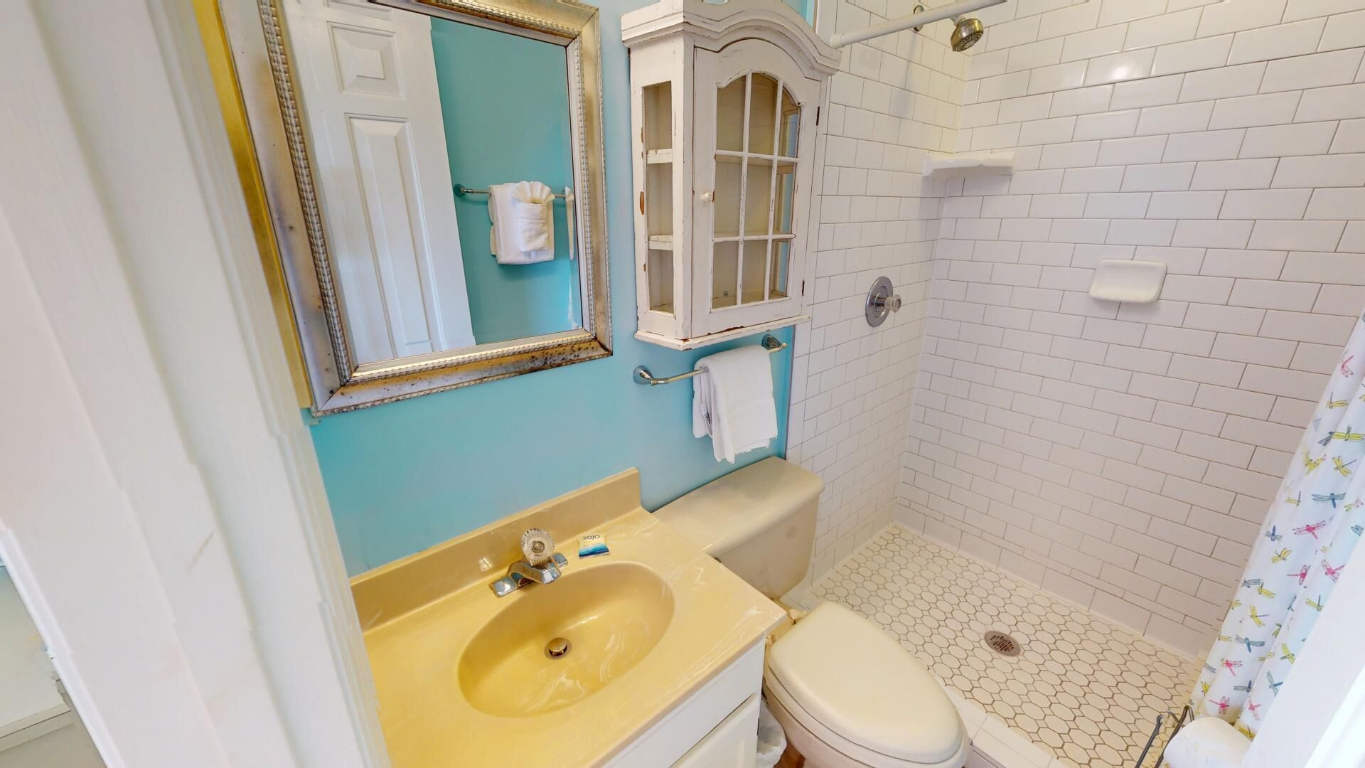 A bathroom with a yellow sink, white toilet, and a shower area with white tiled walls.