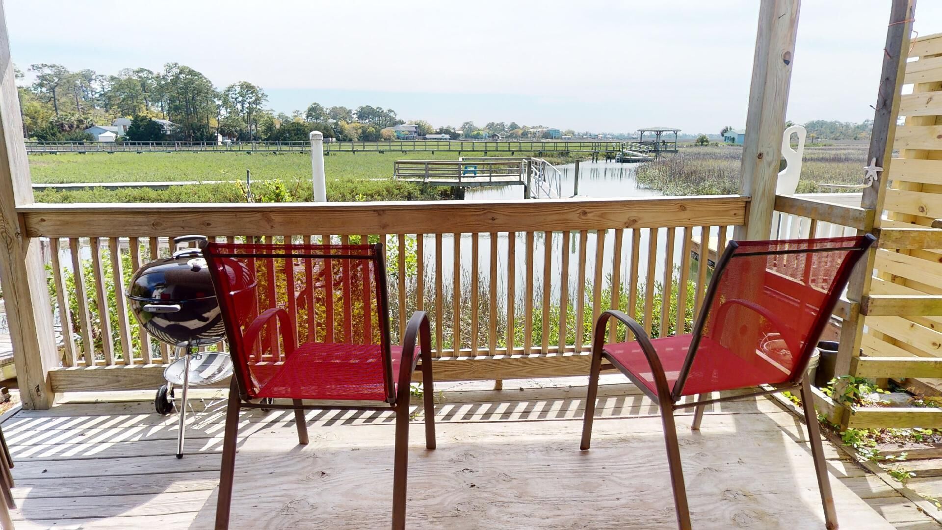 A wooden deck with a grill and two red chairs overlooking a field.