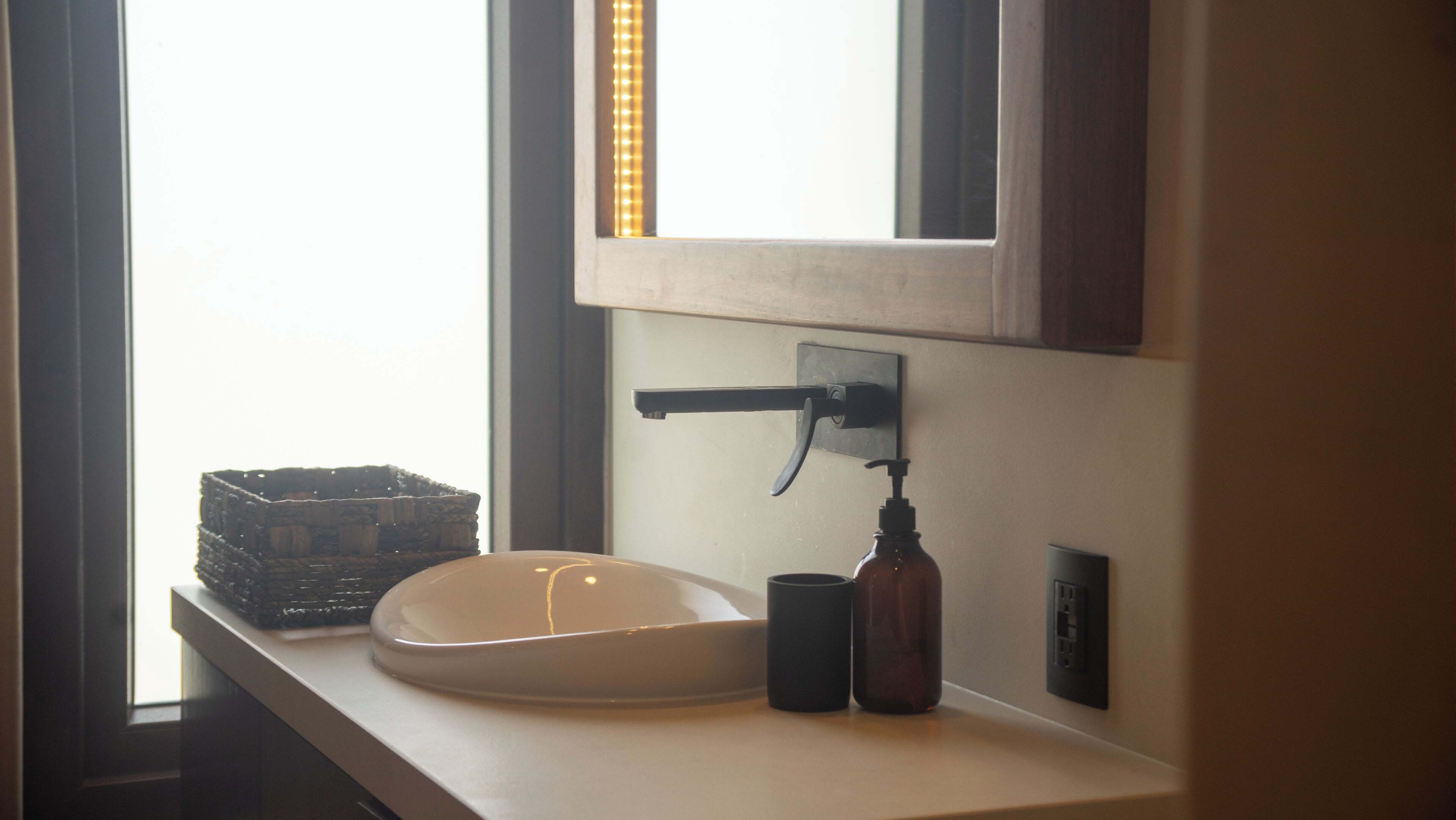 A bathroom sink with a white basin, a black faucet, and a soap dispenser. There is a window with a view of the outside.