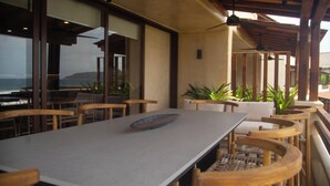 A restaurant with a long table, wooden chairs, and large windows overlooking the ocean. - Minimalist elegance by the beach (Zihuatanejo)