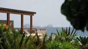 A wooden deck with lounge chairs overlooking a body of water and rocky islands. - Minimalist elegance by the beach (Zihuatanejo)