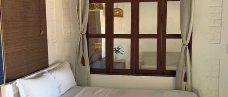 Un dormitorio con cama, mesita de noche, ventana con cortinas y pared con textura.