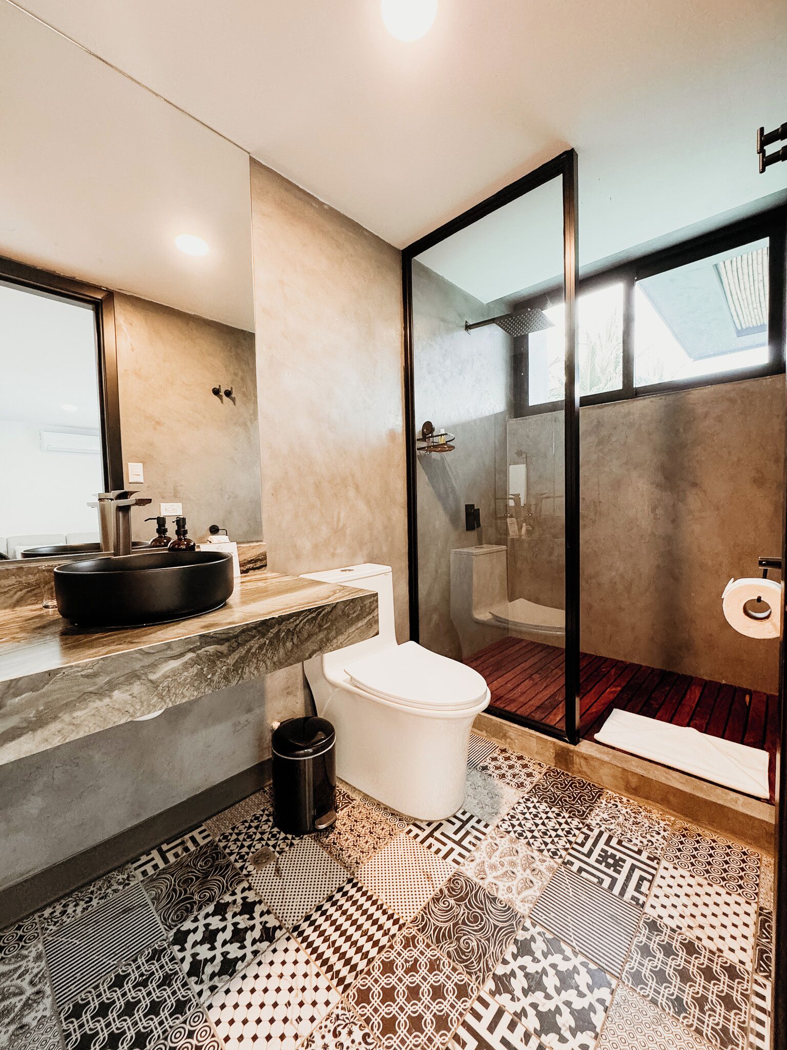 A modern bathroom with a large mirror, a black sink, a toilet, and a patterned floor.
