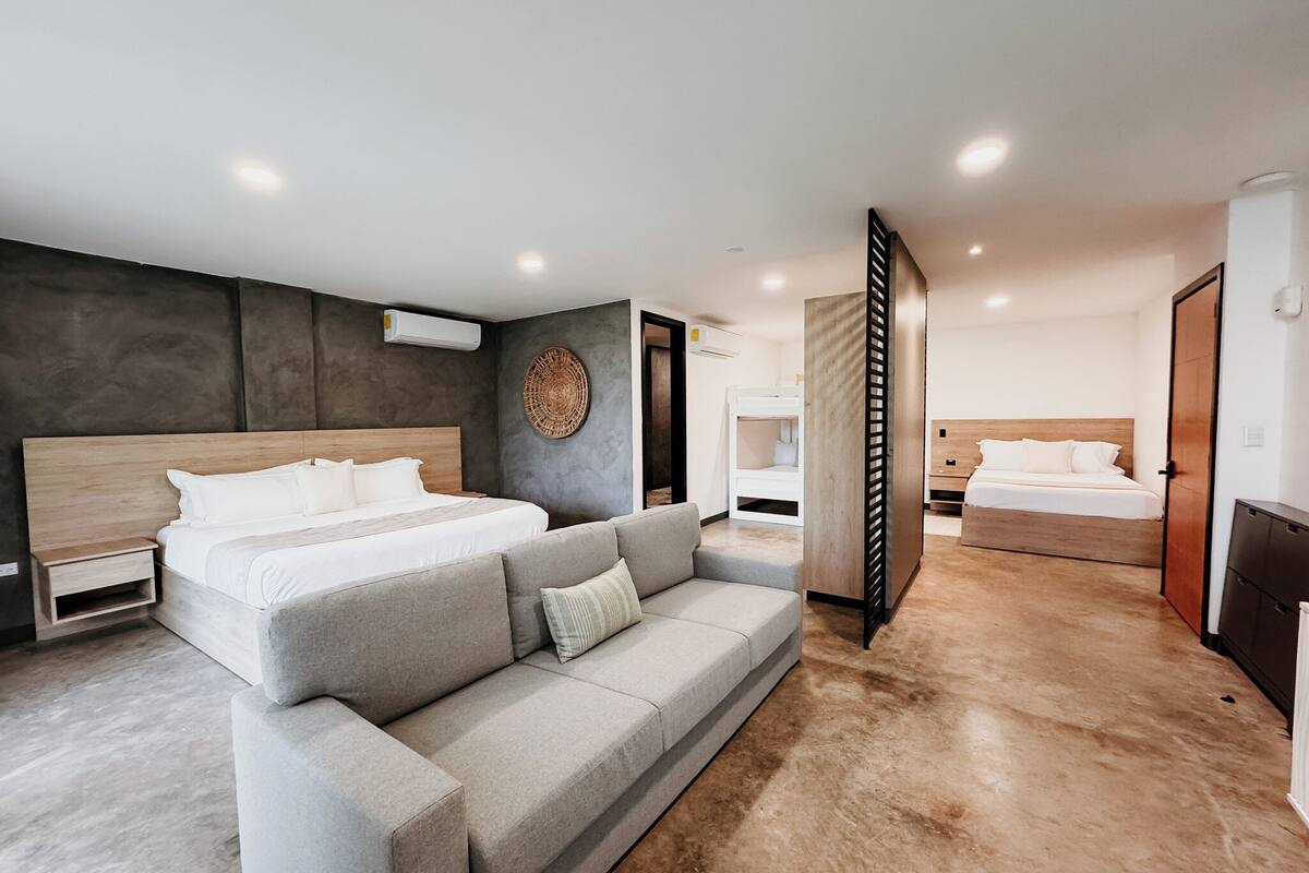 Habitació d'hotel moderna amb un llit gran, un sofà gris i un panell de fusta al capçal.