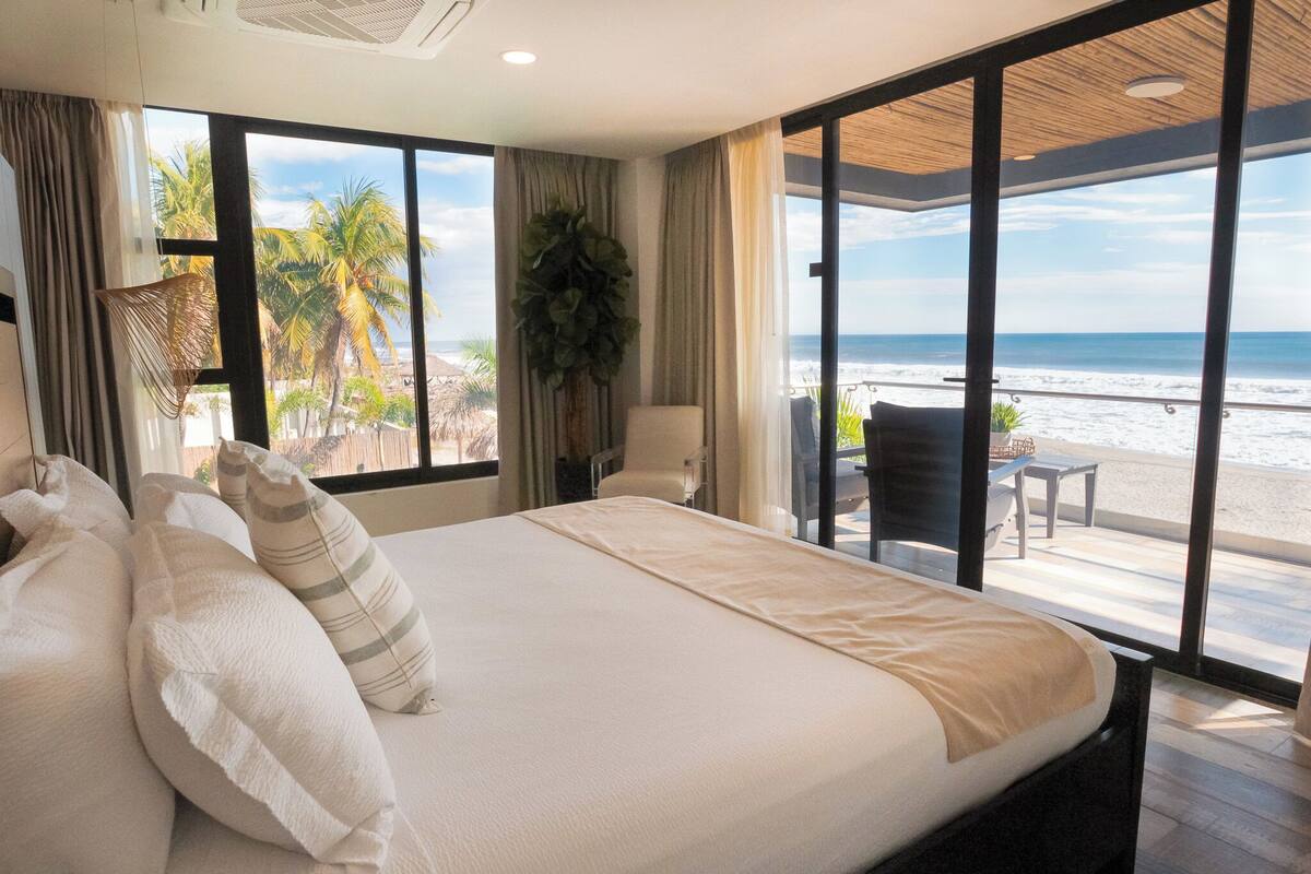 Habitació d'hotel amb un llit gran, vistes a la platja i un balcó amb taula i cadires.