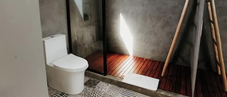 Un baño moderno con inodoro blanco, ducha con puerta de cristal y suelo de madera.
