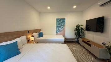 A hotel room with two beds, a TV, a plant, and a painting on the wall.