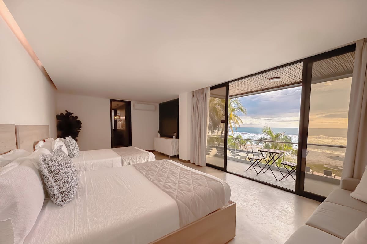 Una habitació d'hotel moderna amb dos llits, un balcó amb vista a la platja i una finestra gran.