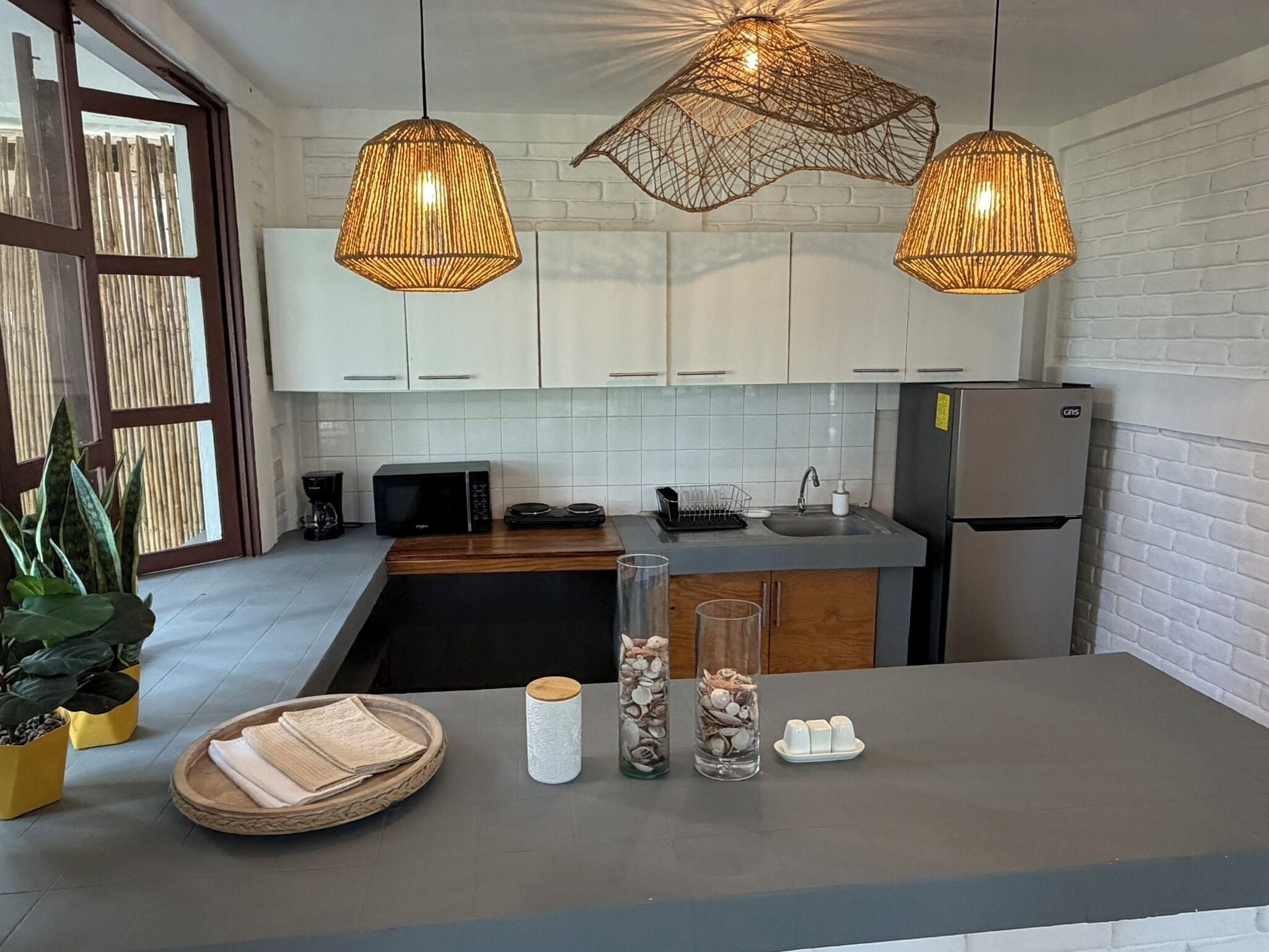 Une cuisine moderne avec des meubles blancs, un micro-ondes noir, un réfrigérateur en acier inoxydable et des suspensions en osier.