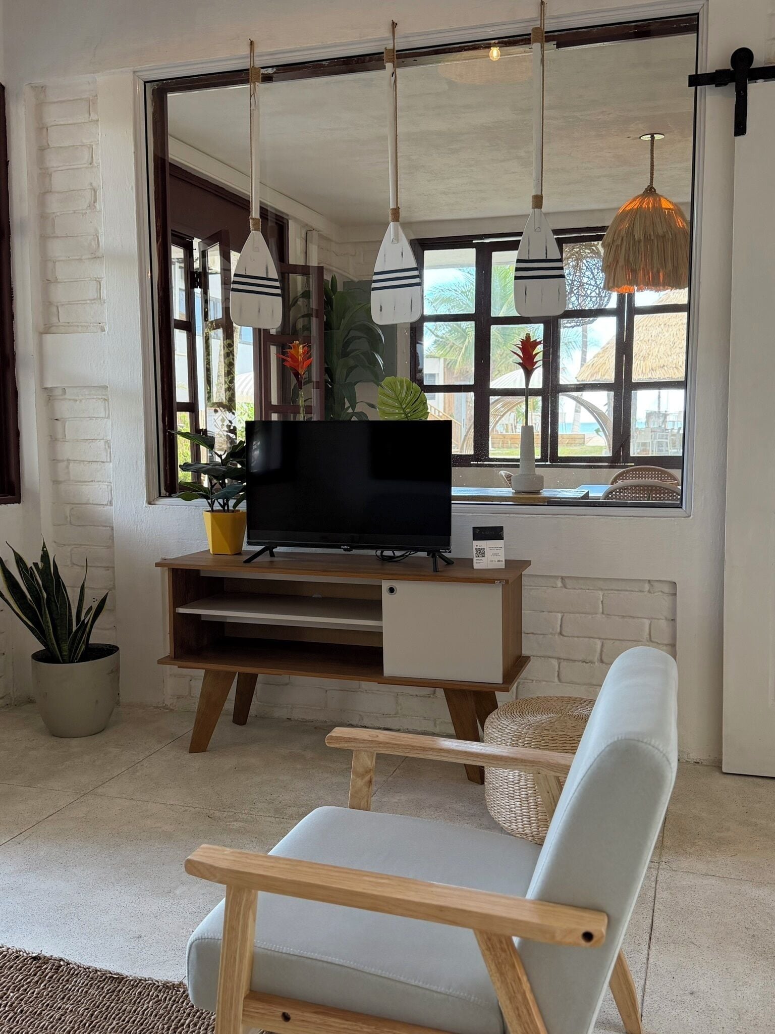 A modern living room with a TV, wooden furniture, hanging lights, and a large window with a view.
