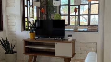 A modern living room with a TV, wooden furniture, hanging lights, and a large window with a view.