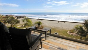 Een balkon met uitzicht op strand en zee. Er staat een tafel met een plant en een stoel.