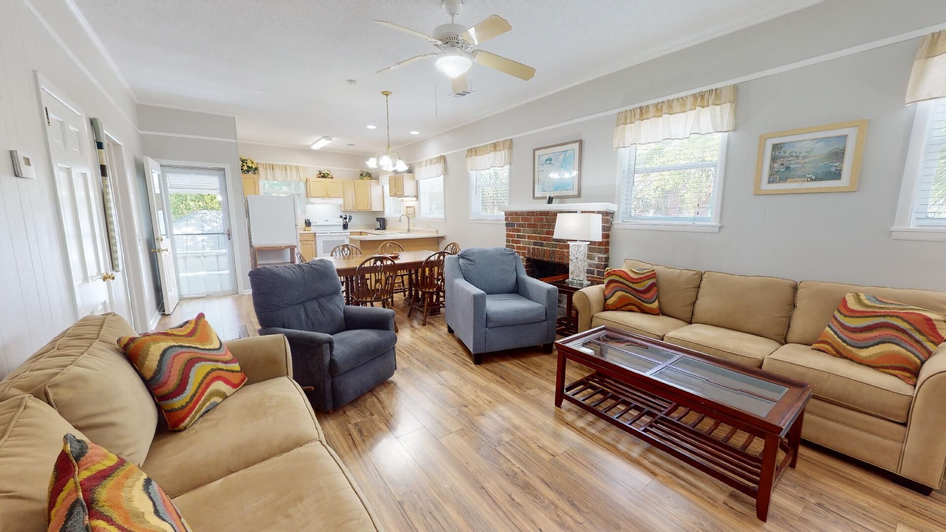 A spacious living room with a fireplace, a dining area, and a kitchen in the background.