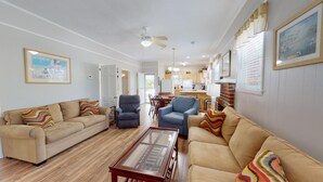 A spacious living room with two beige sofas, a blue armchair, and a wooden coffee table. A kitchen is visible in the background with a dining area. - Beach Nugget by Tybee Vacation Rentals (Tybee Island)