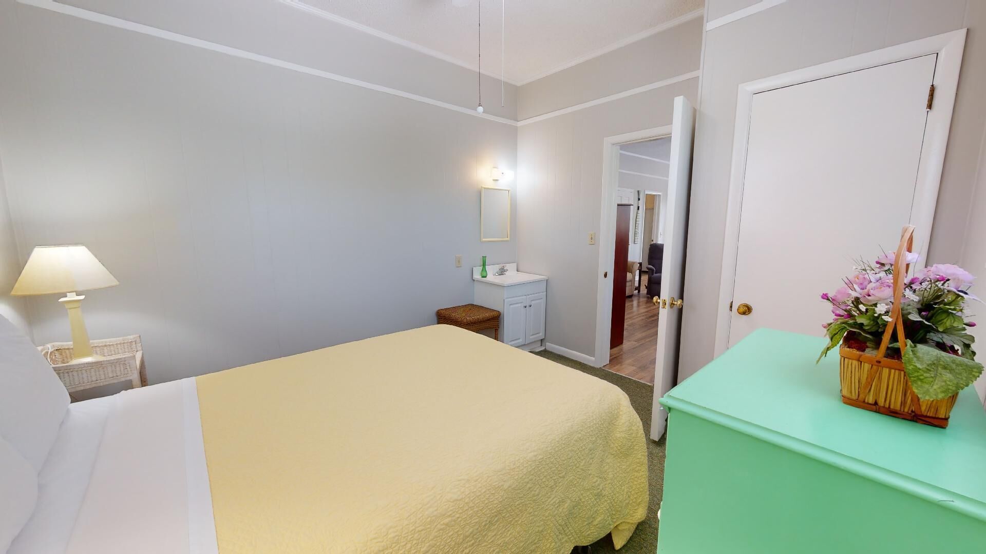 Un dormitorio con cama, mesita de noche, cómoda, espejo y puerta que da a otra habitación.