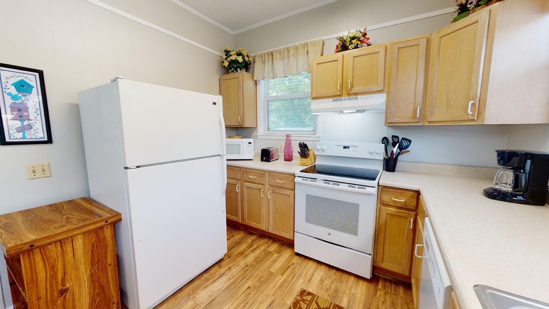 A compact kitchen with wooden cabinets, a white refrigerator, a microwave, a stove, and a coffee maker.
