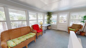 A sunroom with wicker furniture, a table with a lamp, and large windows. - Beach Nugget by Tybee Vacation Rentals (Tybee Island)
