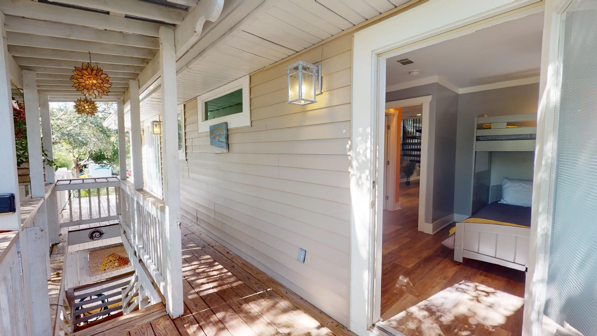 A covered porch with a wooden deck, a small outdoor seating area, and a view into a room with bunk beds.