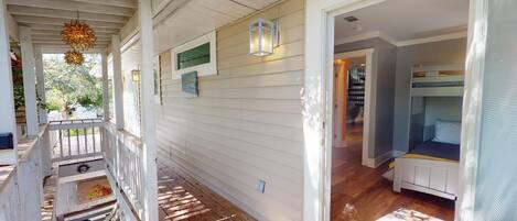 A covered porch with a wooden deck, a small outdoor seating area, and a view into a room with bunk beds.