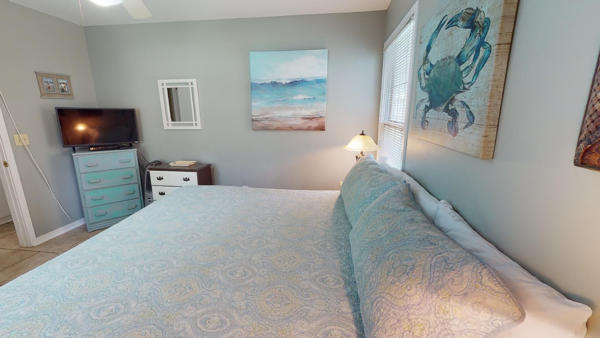 A bedroom with a bed, a dresser, a TV, and artwork on the walls.