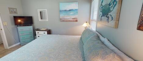 A bedroom with a bed, a dresser, a TV, and artwork on the walls.