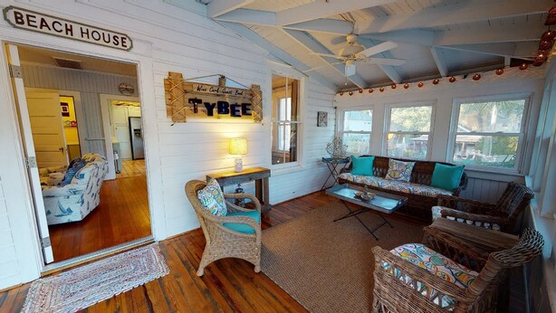 A cozy interior with a wicker sofa, a wooden table, and a wicker chair. A sign reads "BEACH HOUSE" and another says "Tybee."