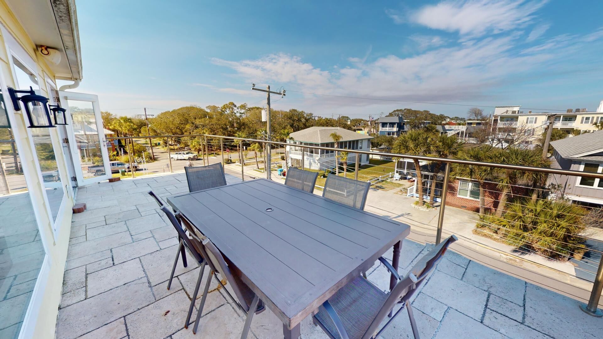 Uma varanda com mesa e cadeiras, com vista para uma área residencial com casas e árvores.