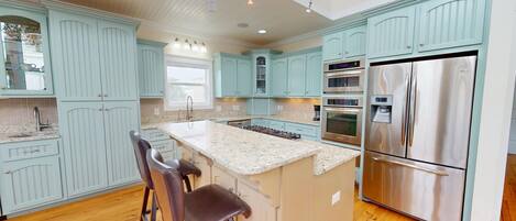 A kitchen with light blue cabinets, a stainless steel refrigerator, and a granite countertop.