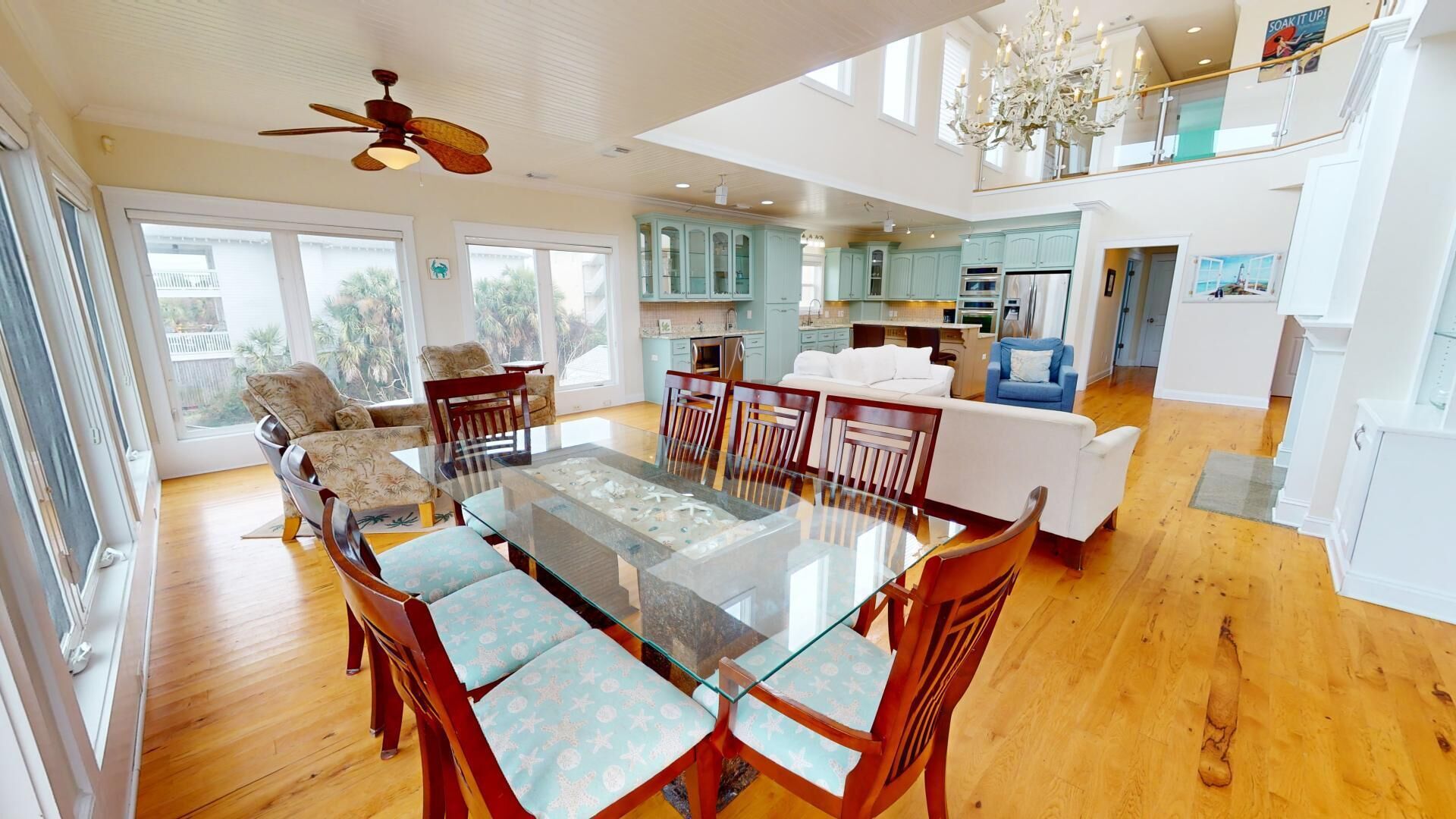 A spacious living area with a glass dining table, wooden chairs, a sofa, and a ceiling fan.