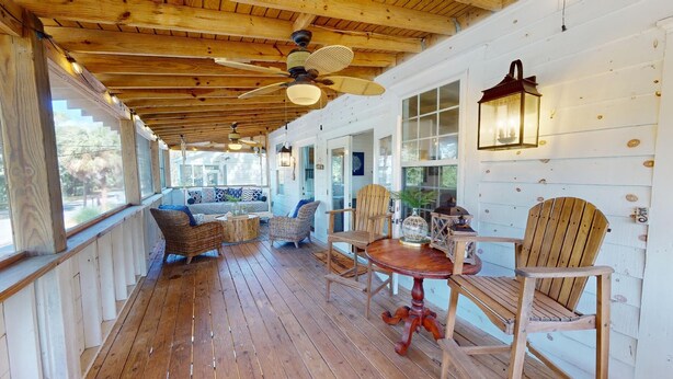 Une terrasse en bois avec un ventilateur de plafond, des meubles en osier et une lanterne.