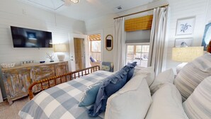 Une chambre à coucher avec un grand lit, une commode en bois, un téléviseur et une fenêtre avec des rideaux.