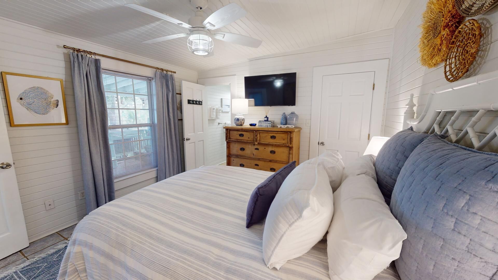 A bedroom with a bed, a ceiling fan, a dresser, a TV, and a door.
